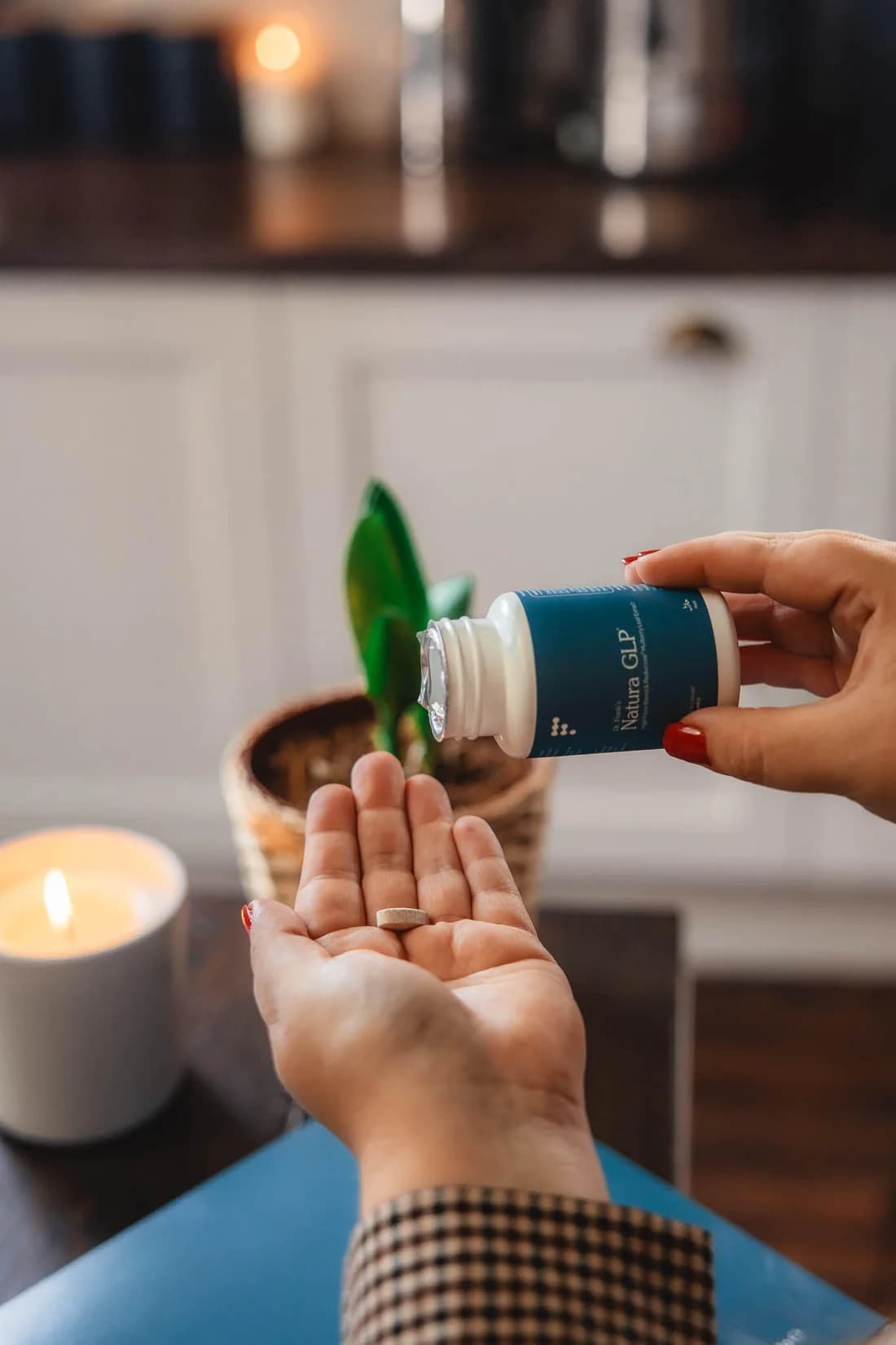 A hand offers a Natura bottle over an open palm beside a lit candle.