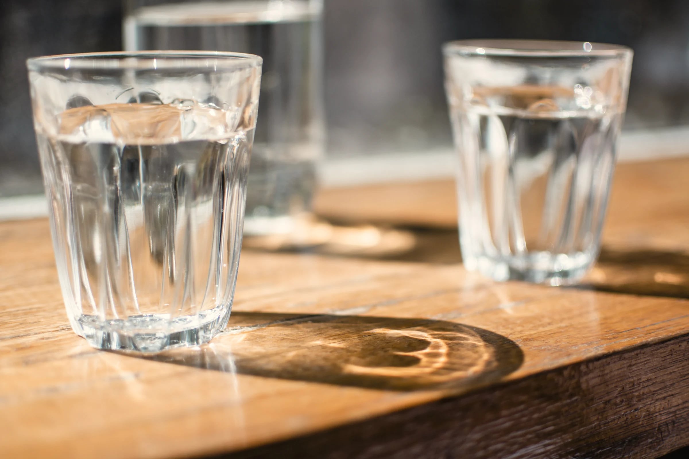 Two glasses of water on a wooden table in afternoon sun