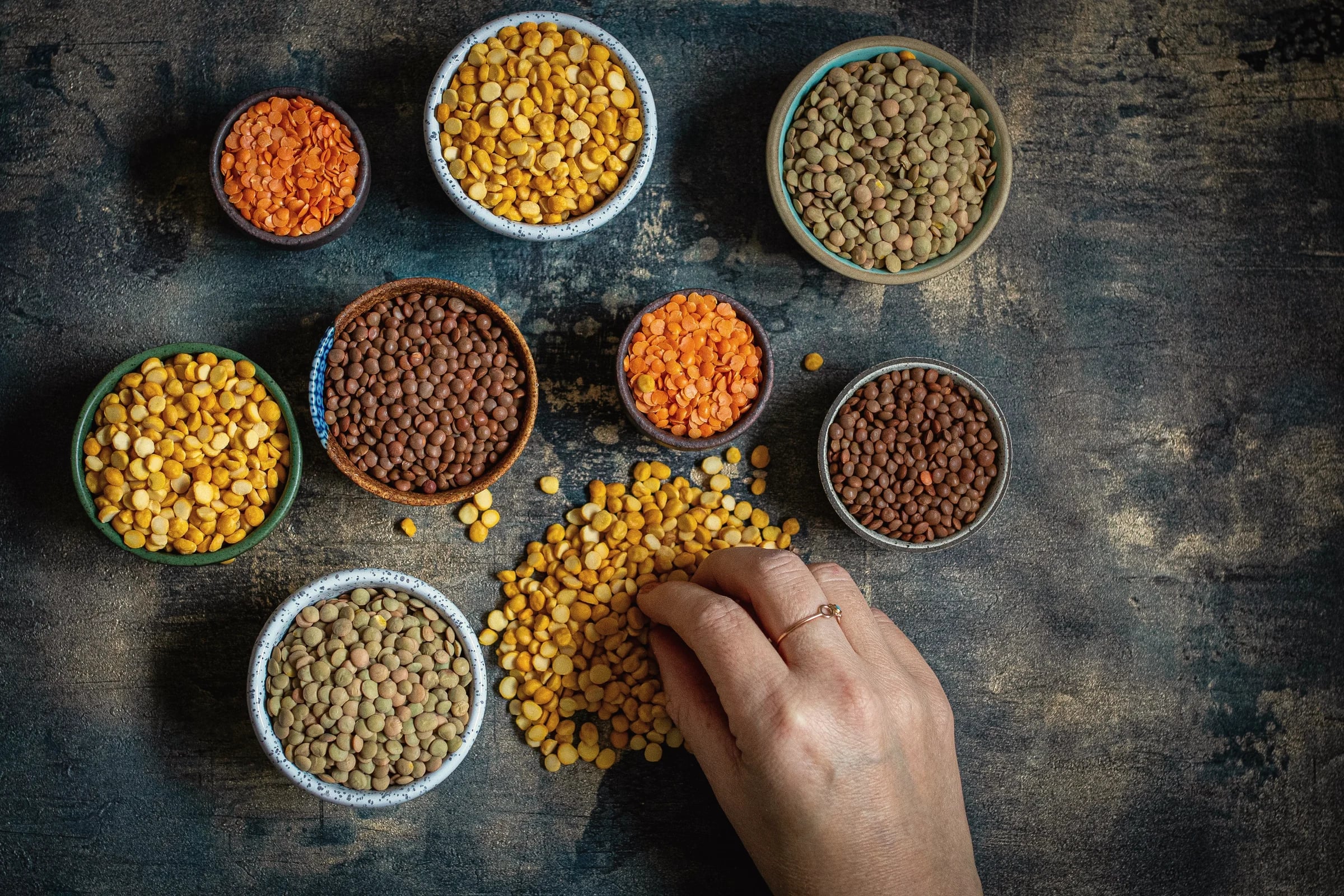 Bowls of lentils and split peas with a hand sorting them