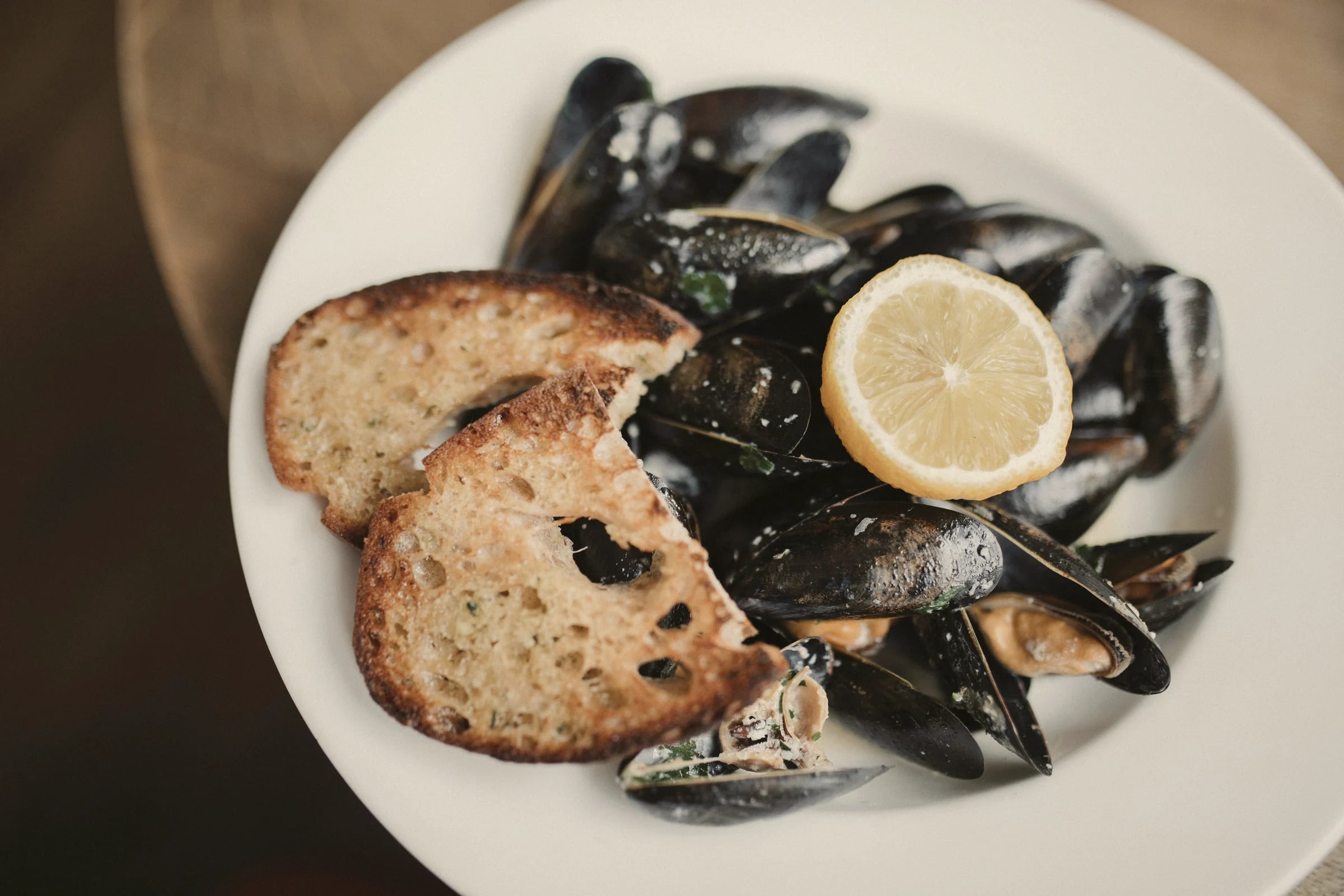 A plate of mussels with toasted bread and a slice of lemon