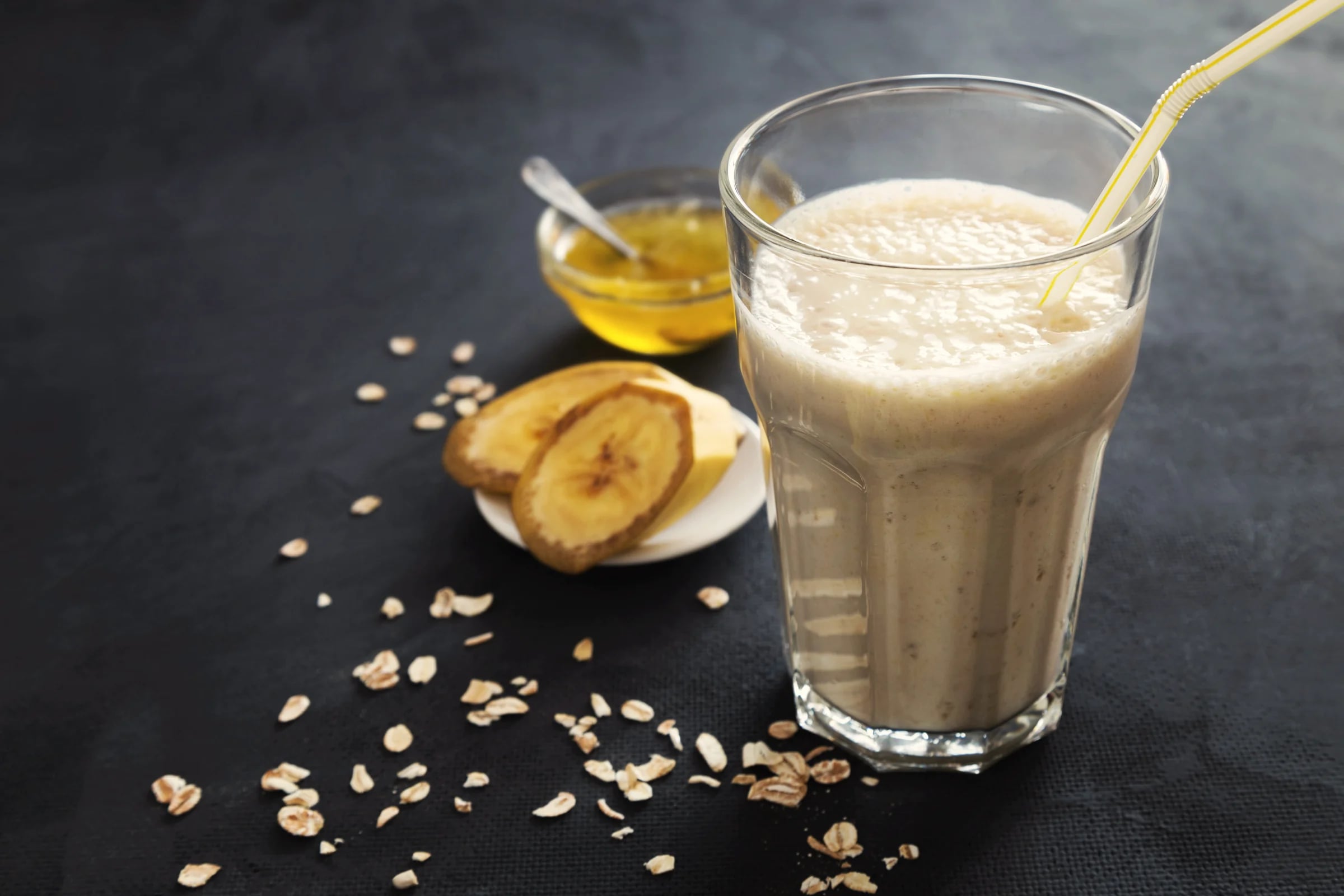 A banana and oat smoothie in a glass with oats and honey