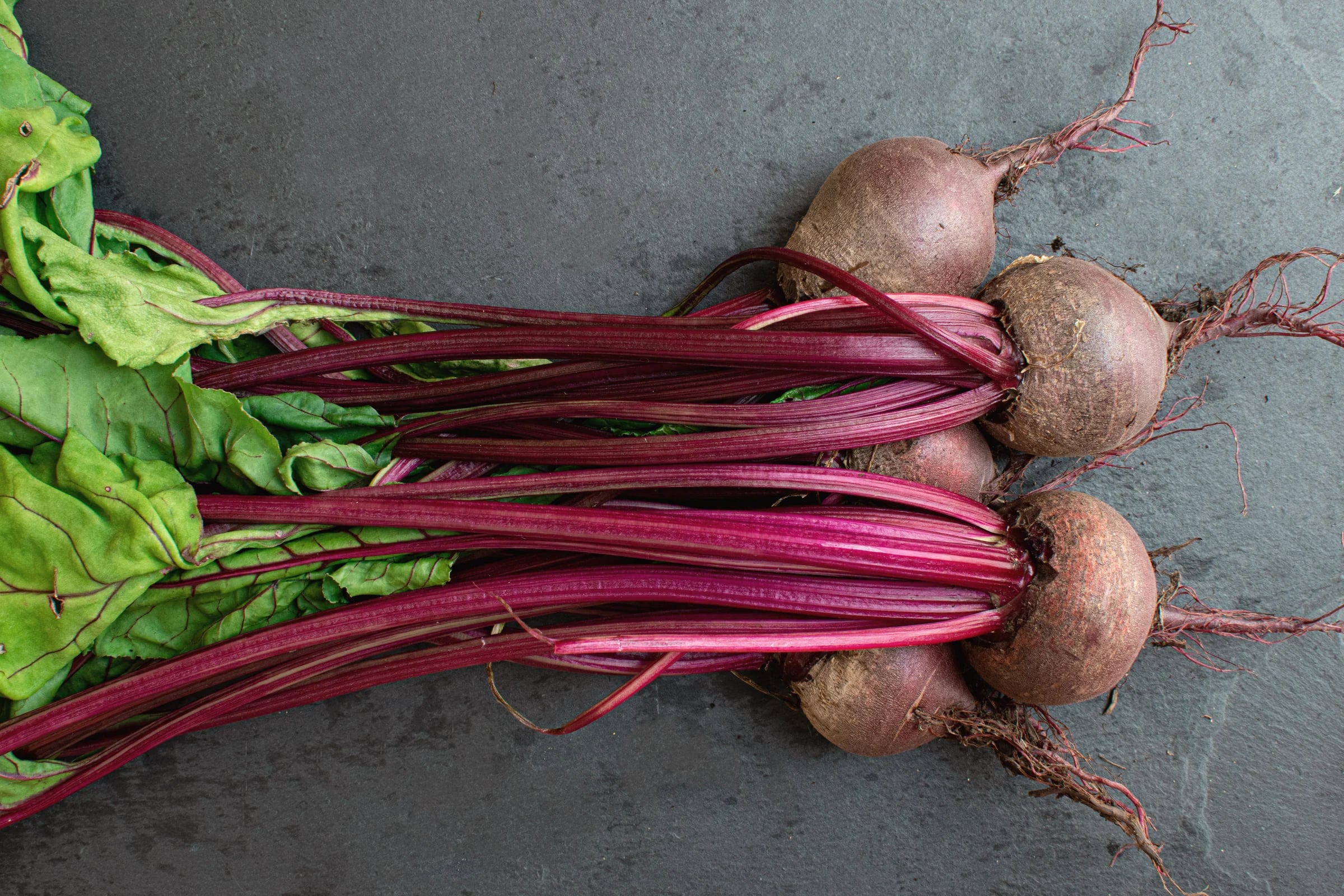 A bunch of fresh beetroot with its leaves on dark slate
