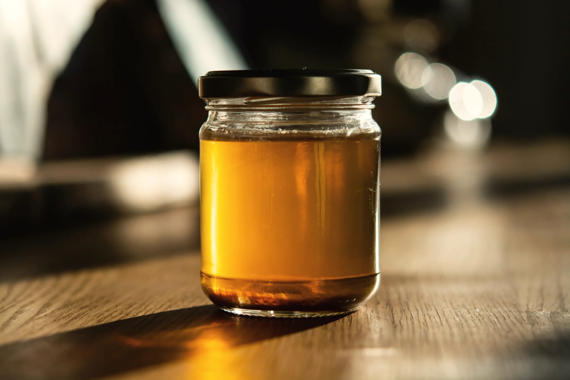 A jar of golden broth on a wooden table in warm light