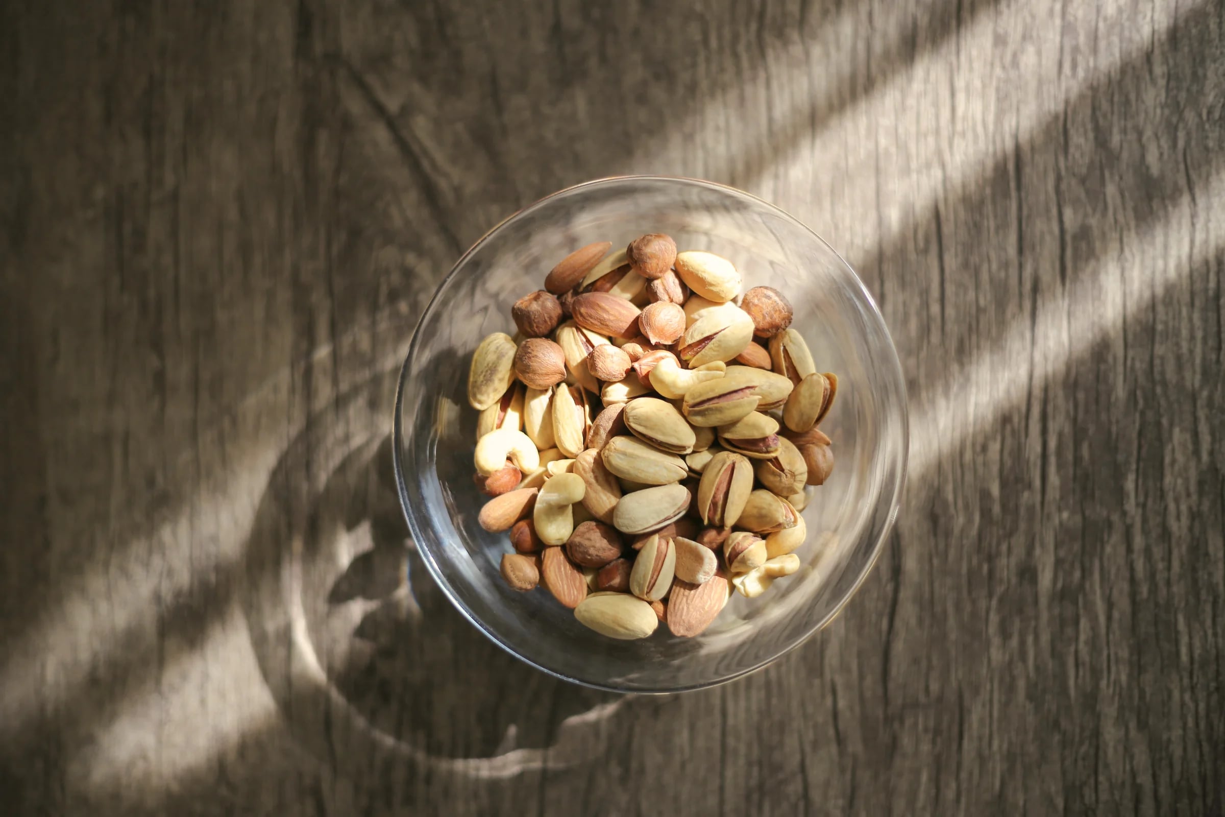 A glass bowl of mixed nuts in a stripe of sunlight