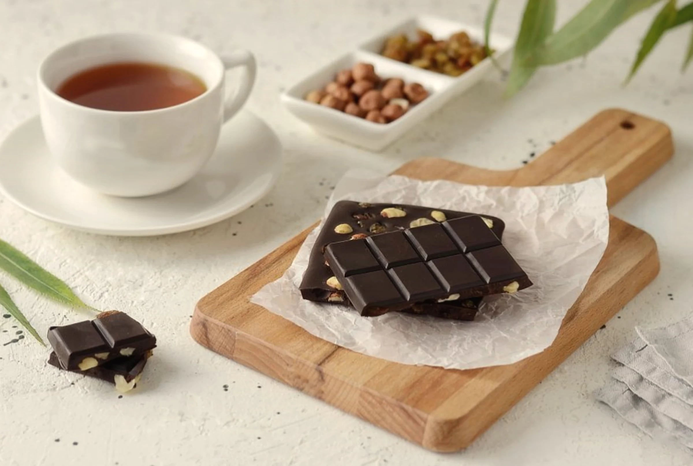 Squares of dark chocolate on a board beside a cup of tea and nuts