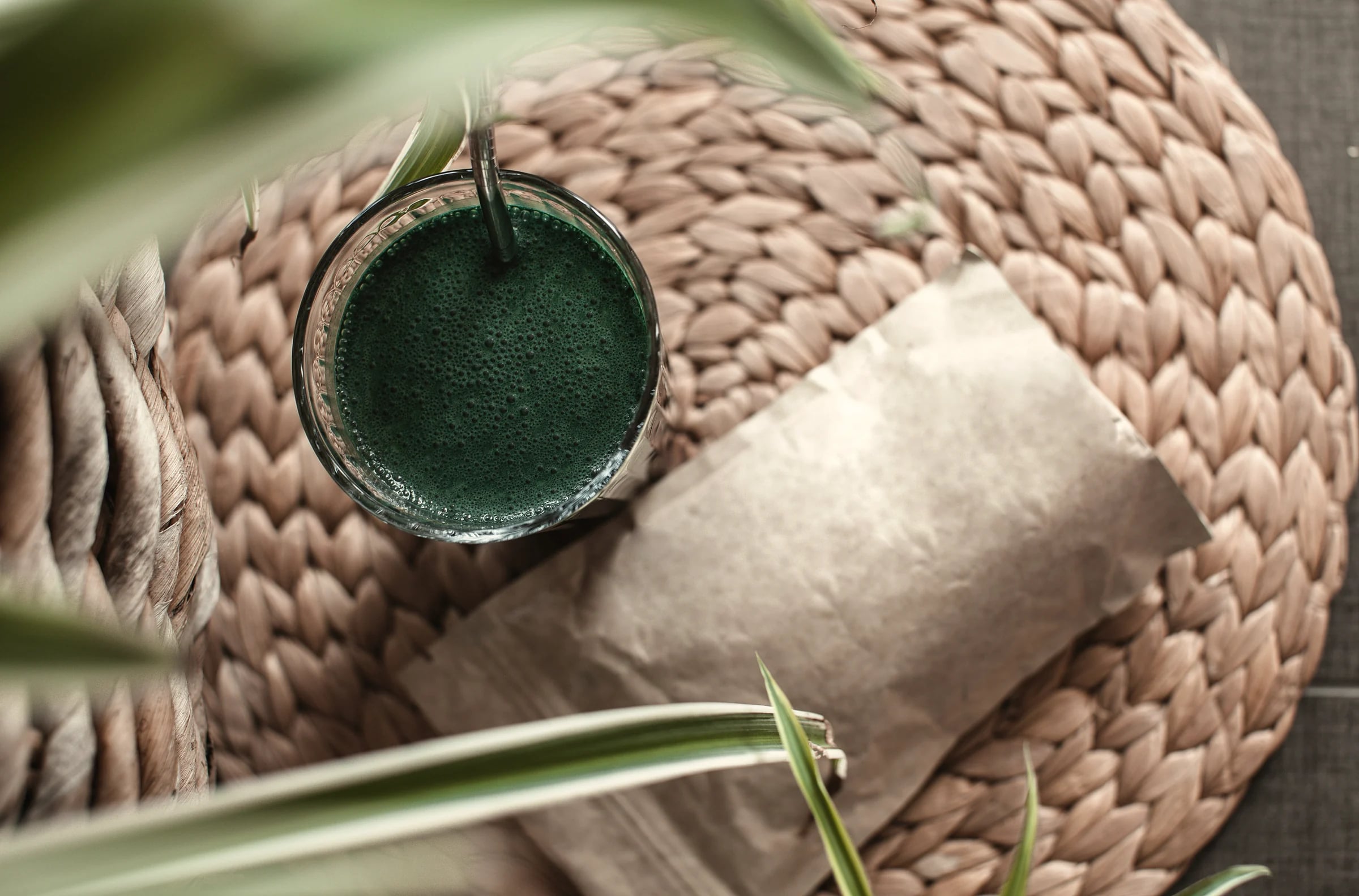 A glass of deep green spirulina drink on a woven mat
