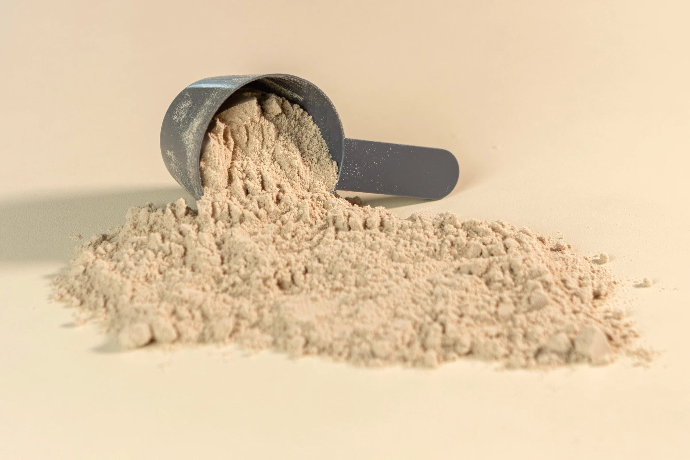 A scoop of protein powder spilling onto a pale surface